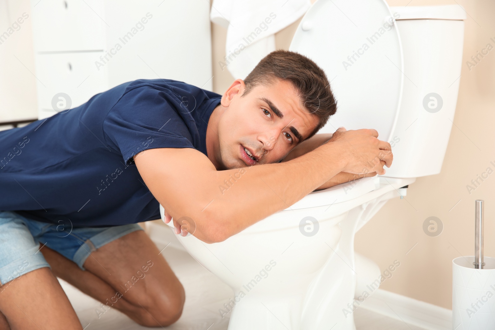 Photo of Young man vomiting in toilet bowl at home