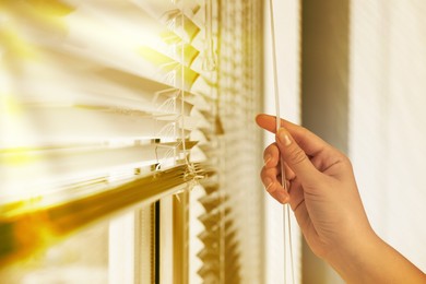 Image of Woman opening horizontal blinds on window indoors, closeup