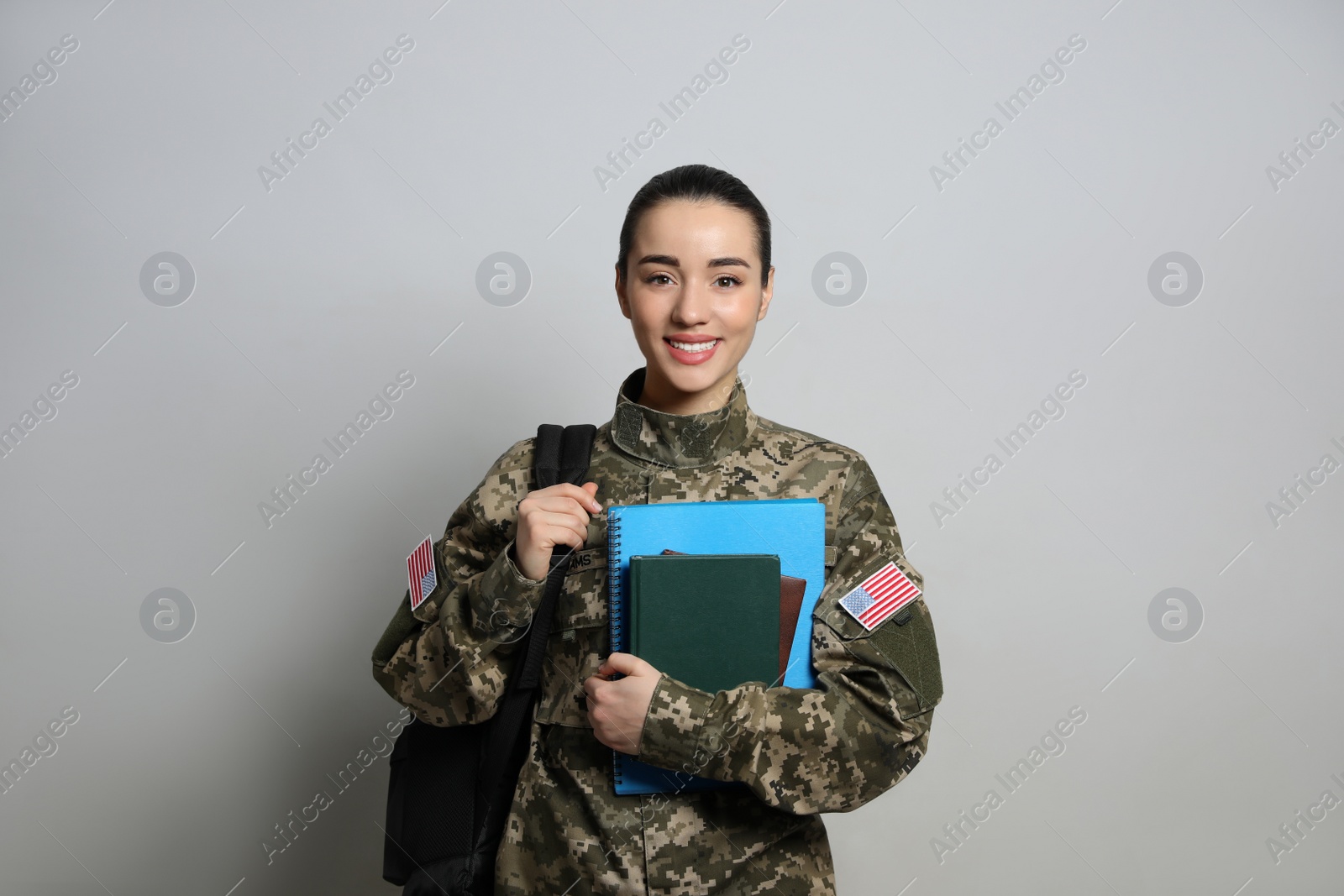 Photo of Female soldier with notebooks and backpack on light grey background. Military education