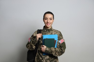 Photo of Female soldier with notebooks and backpack on light grey background. Military education