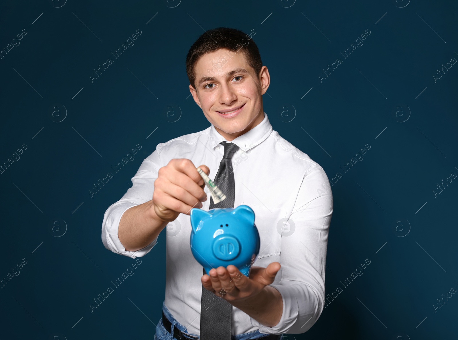 Photo of Businessman putting money into piggy bank on color background