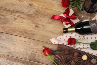 Photo of Red wine, chocolate truffles, gift box and roses on wooden table, flat lay. Space for text