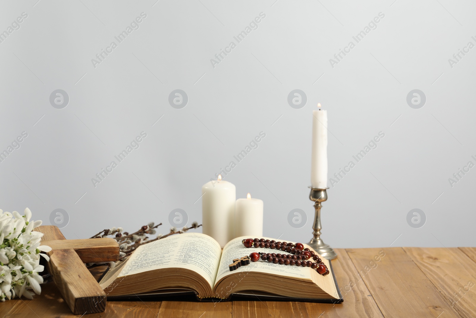 Photo of Church candles, cross, rosary beads, Bible and willow branches on wooden table against light background. Space for text