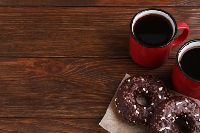 Photo of Two frosted donuts with sprinkles and cups of coffee on wooden table, space for text