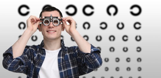 Vision test. Young man with trial frame and eye chart on gradient background. Banner design