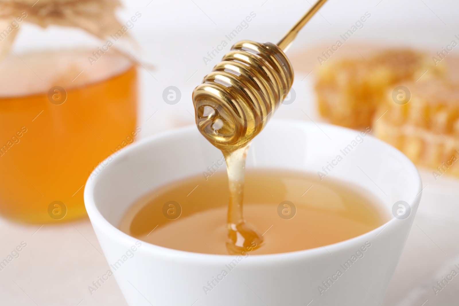 Photo of Dripping tasty honey from dipper into bowl on table, closeup