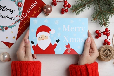 Photo of Woman holding Christmas card at white wooden table, top view