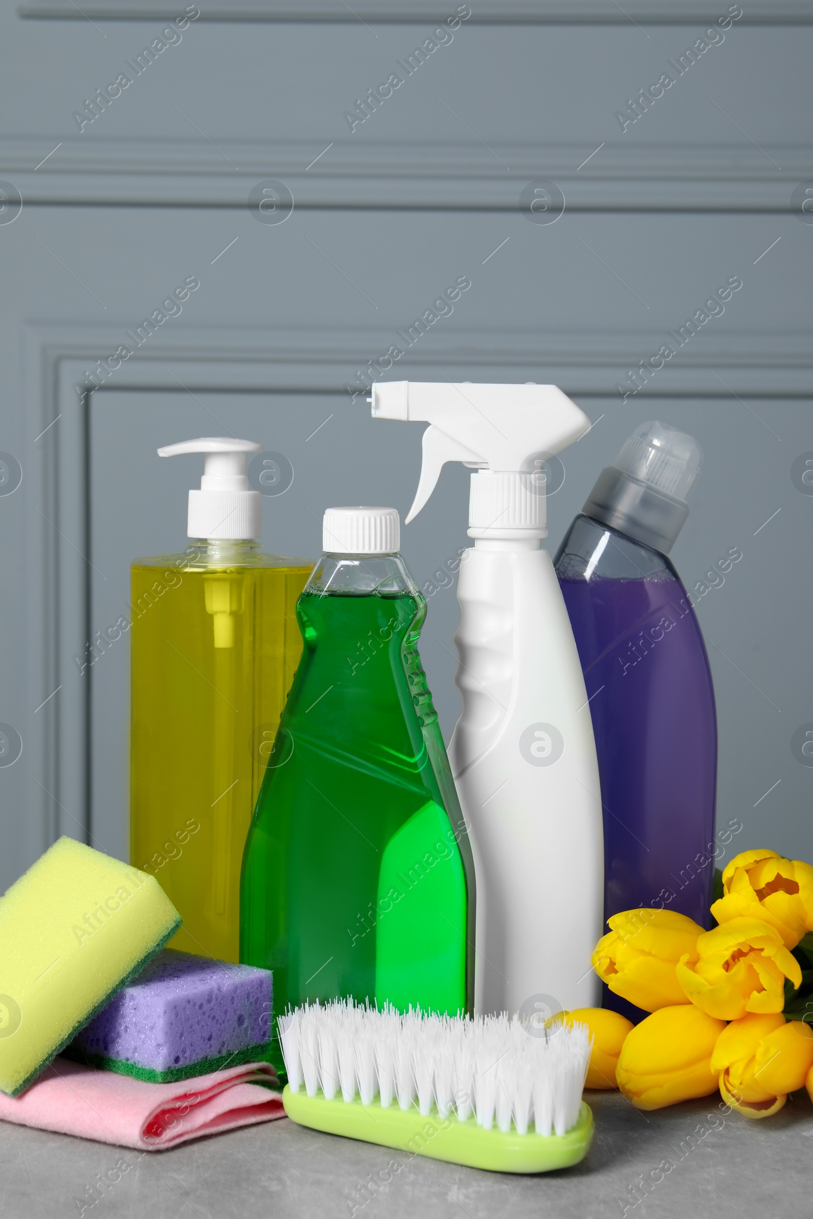 Photo of Spring cleaning. Detergents, flowers and tools on grey textured table