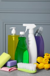 Photo of Spring cleaning. Detergents, flowers and tools on grey textured table