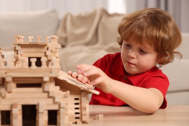 Cute little boy playing with wooden castle at table in room. Child's toy