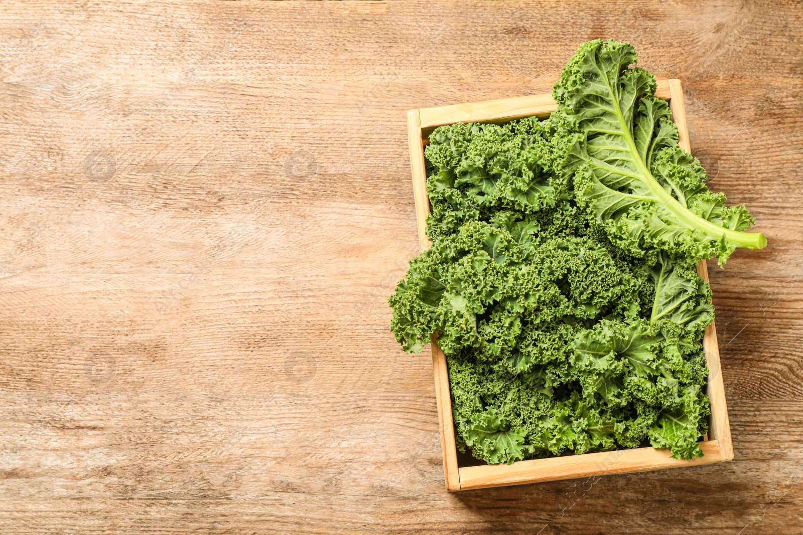 Photo of Fresh kale leaves on wooden table, top view. Space for text