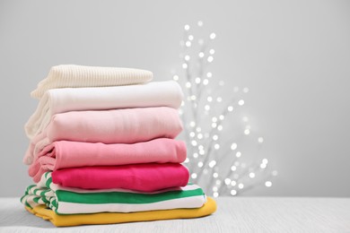 Photo of Stack of folded clothes on wooden table against beige background with blurred lights, space for text