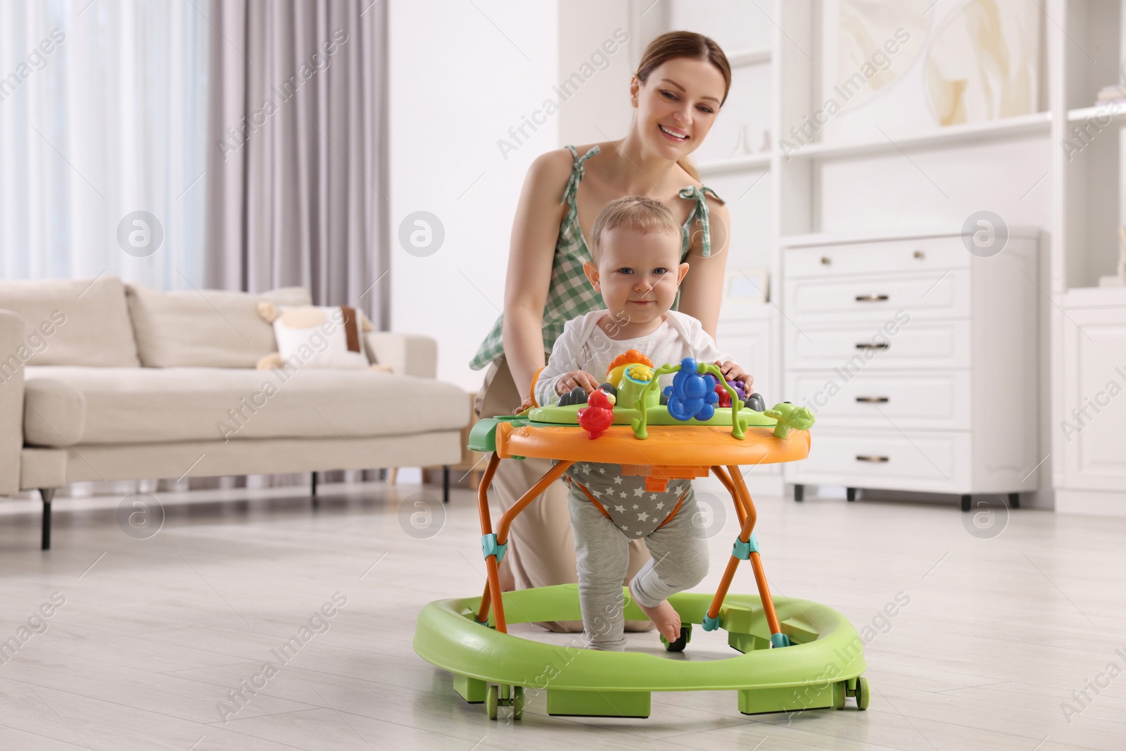 Photo of Cute boy making first steps with baby walker. Happy mother and her little son spending time together at home