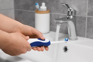 Photo of Woman holding electric toothbrush above sink in bathroom, closeup