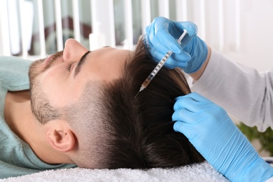 Photo of Young man with hair loss problem receiving injection in salon