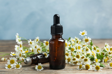 Bottles of essential oil and fresh chamomiles on wooden table