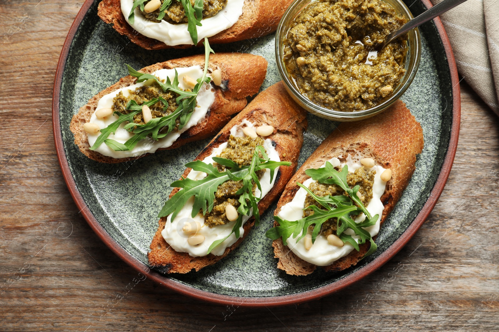 Photo of Plate with tasty bruschettas and pesto sauce on wooden table, top view