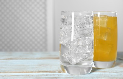 Photo of Glasses of different refreshing soda water with ice cubes on light blue wooden table, space for text