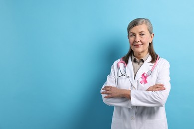 Photo of Mammologist with pink ribbon on light blue background, space for text. Breast cancer awareness