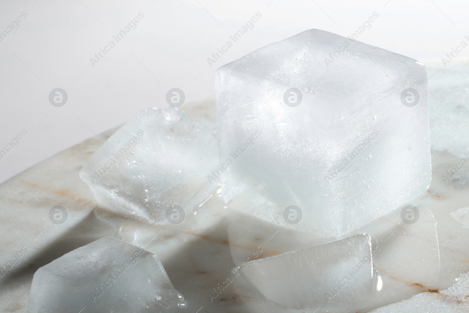 Photo of Crystal clear ice cubes on light grey marble board, closeup