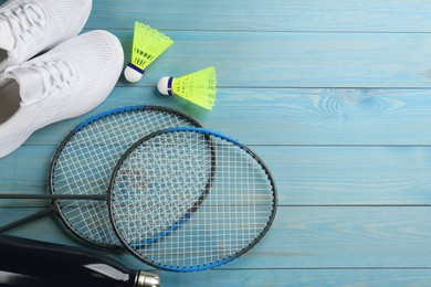 Photo of Rackets, shoes and shuttlecocks on light blue wooden table, space for text. Playing badminton