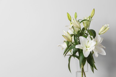 Beautiful bouquet of lily flowers in glass vase on white background, space for text