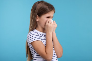 Photo of Sick girl with tissue coughing on light blue background