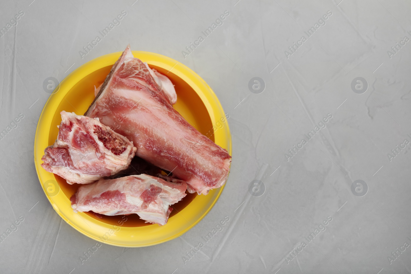 Photo of Feeding bowl with raw chopped meaty bones on grey table, top view. Space for text