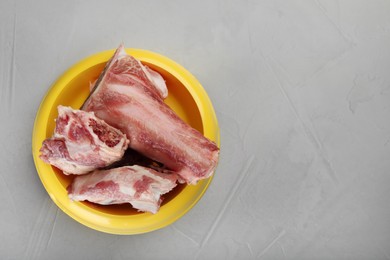 Photo of Feeding bowl with raw chopped meaty bones on grey table, top view. Space for text