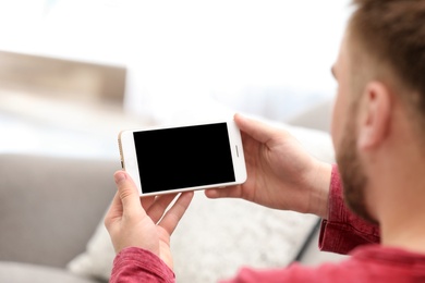 Young man using video chat on smartphone in living room, closeup. Space for design