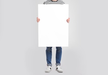 Man holding blank poster on light grey background, closeup