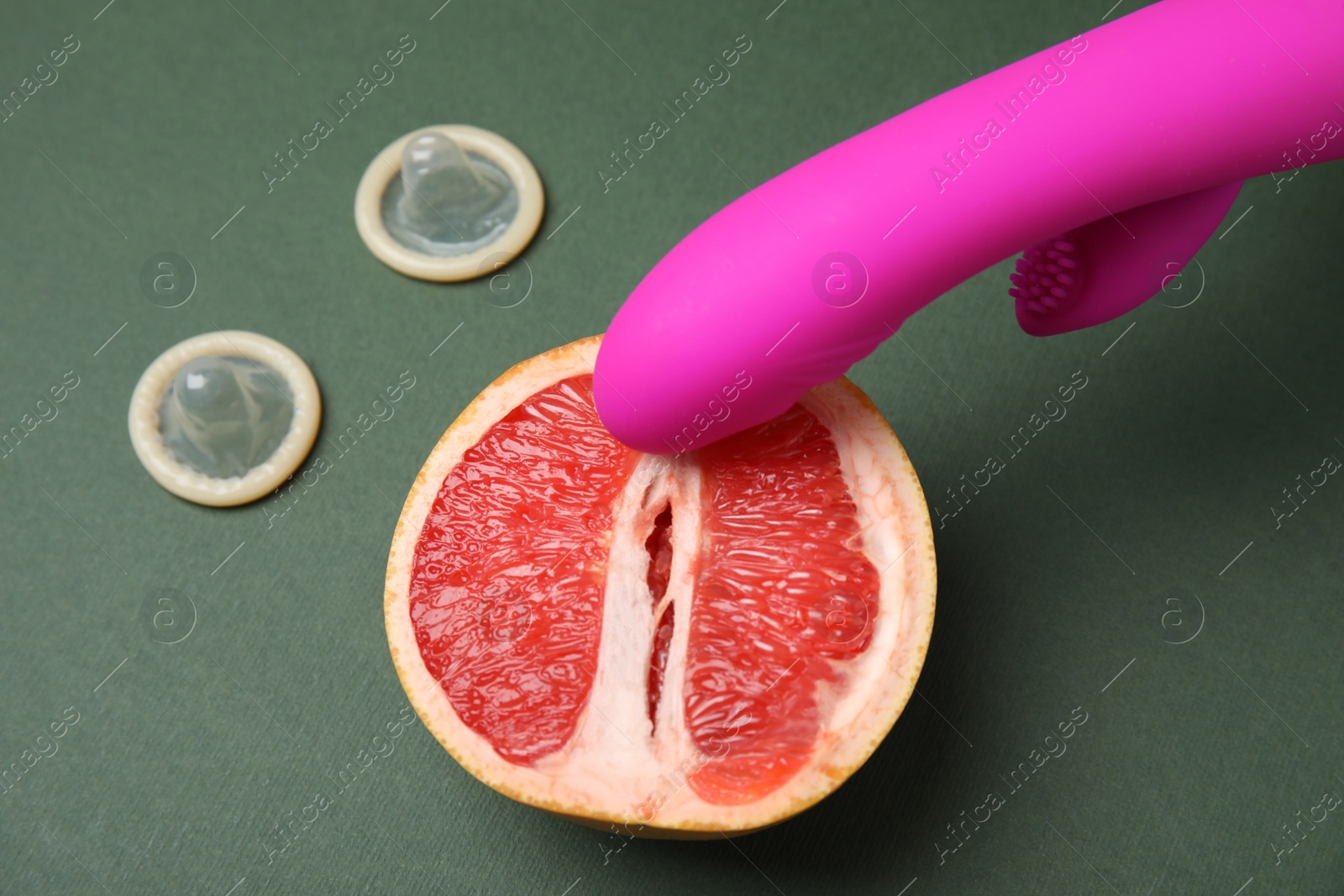 Photo of Half of grapefruit, purple vibrator and condoms on dark grey background. Sex concept