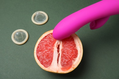 Half of grapefruit, purple vibrator and condoms on dark grey background. Sex concept