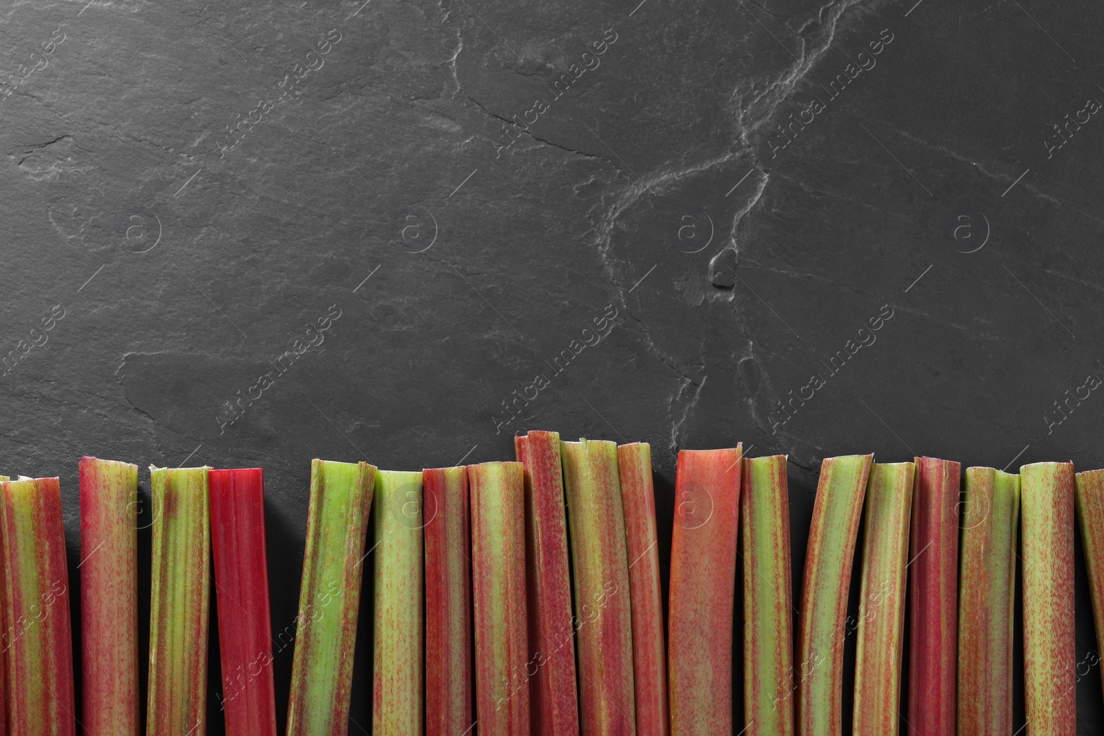 Photo of Fresh ripe rhubarb stalks on grey textured table, top view. Space for text