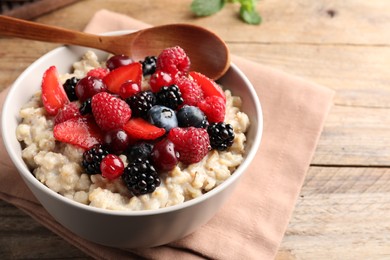 Photo of Bowl with tasty oatmeal porridge and berries served on wooden table, closeup. Healthy meal