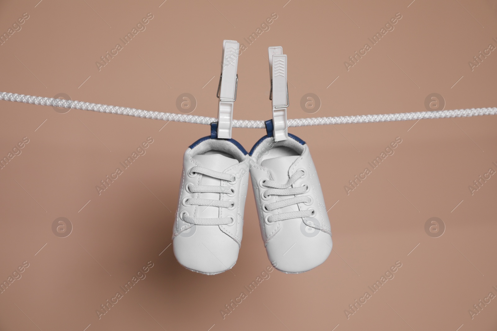 Photo of Cute small baby shoes hanging on washing line against brown background