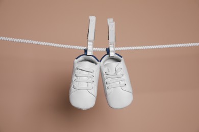 Cute small baby shoes hanging on washing line against brown background