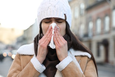 Photo of Woman with tissue blowing runny nose outdoors. Cold symptom