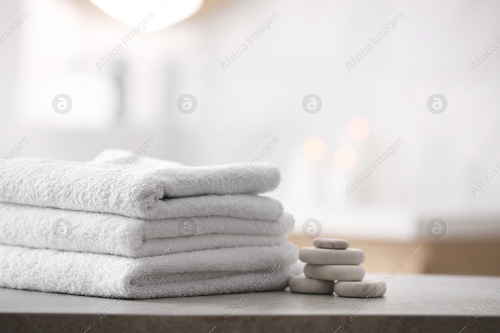 Photo of Stack of fresh towels and spa stones on table in bathroom