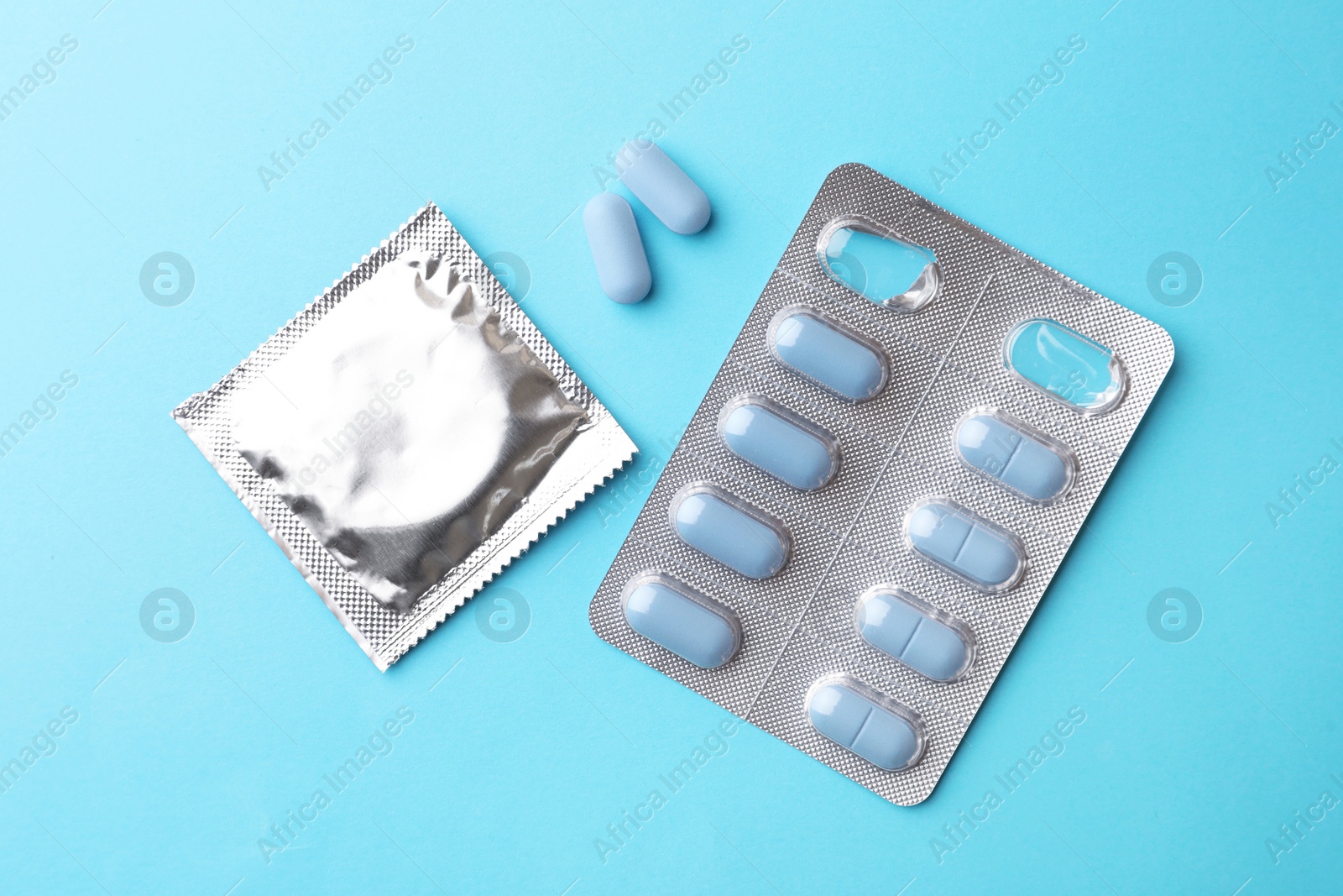 Photo of Pills and condom on light blue background, flat lay. Potency problem