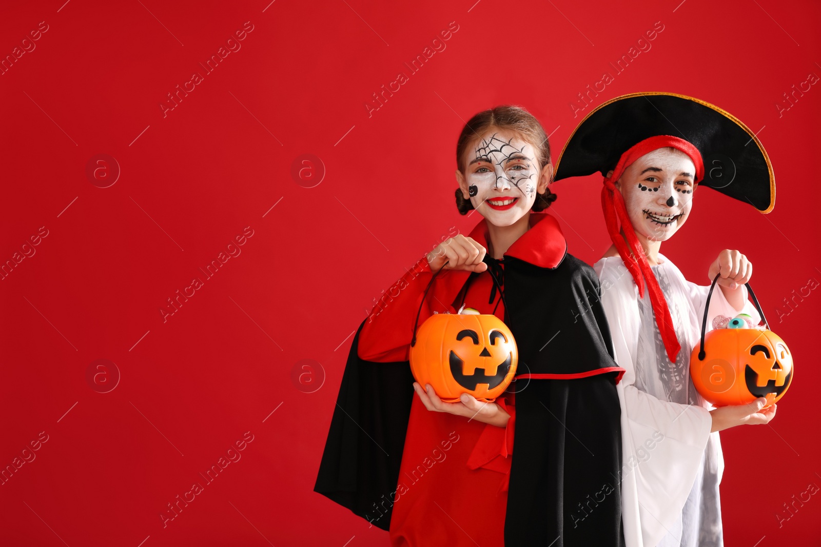 Photo of Cute little kids with pumpkin candy buckets wearing Halloween costumes on red background. Space for text