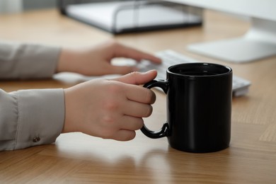 Woman with black ceramic mug at workplace, closeup