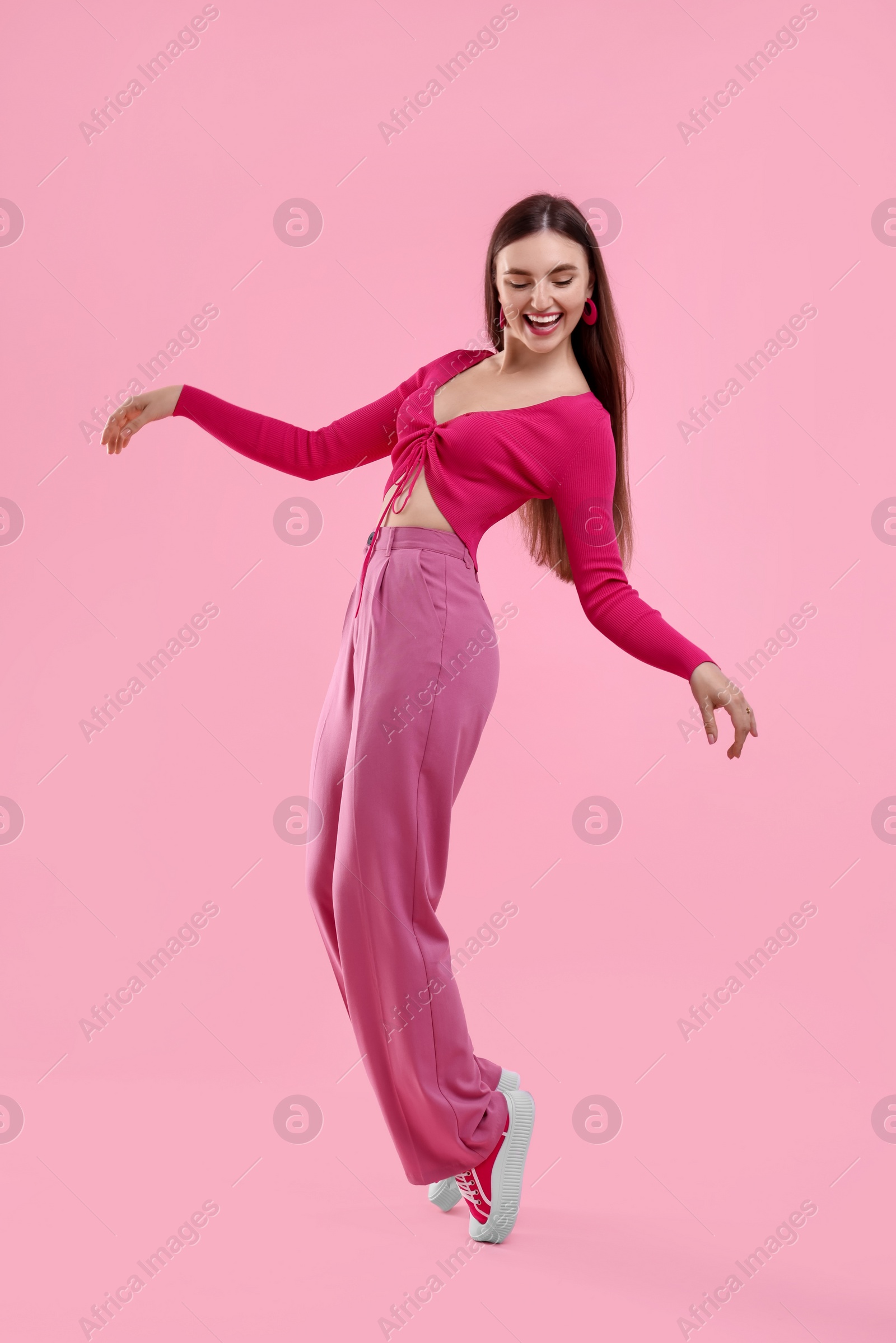 Photo of Beautiful young woman in pink clothes dancing on color background