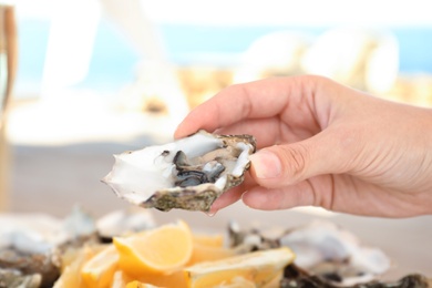 Photo of Woman holding fresh oyster over plate, focus on hand