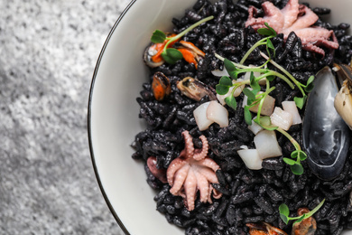 Delicious black risotto with seafood in bowl on table, closeup