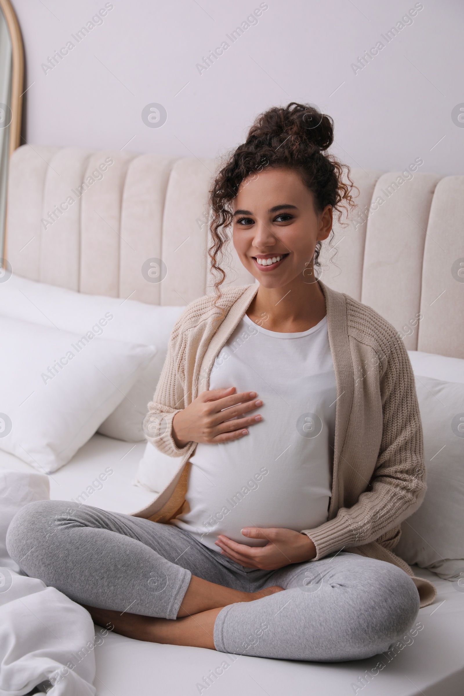 Photo of Pregnant young African-American woman sitting on bed at home