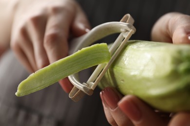 Photo of Woman peeling fresh zucchini indoors, closeup view
