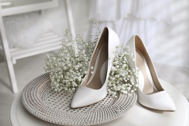 Photo of Beautiful wedding shoes, engagement ring and flowers on table indoors, closeup