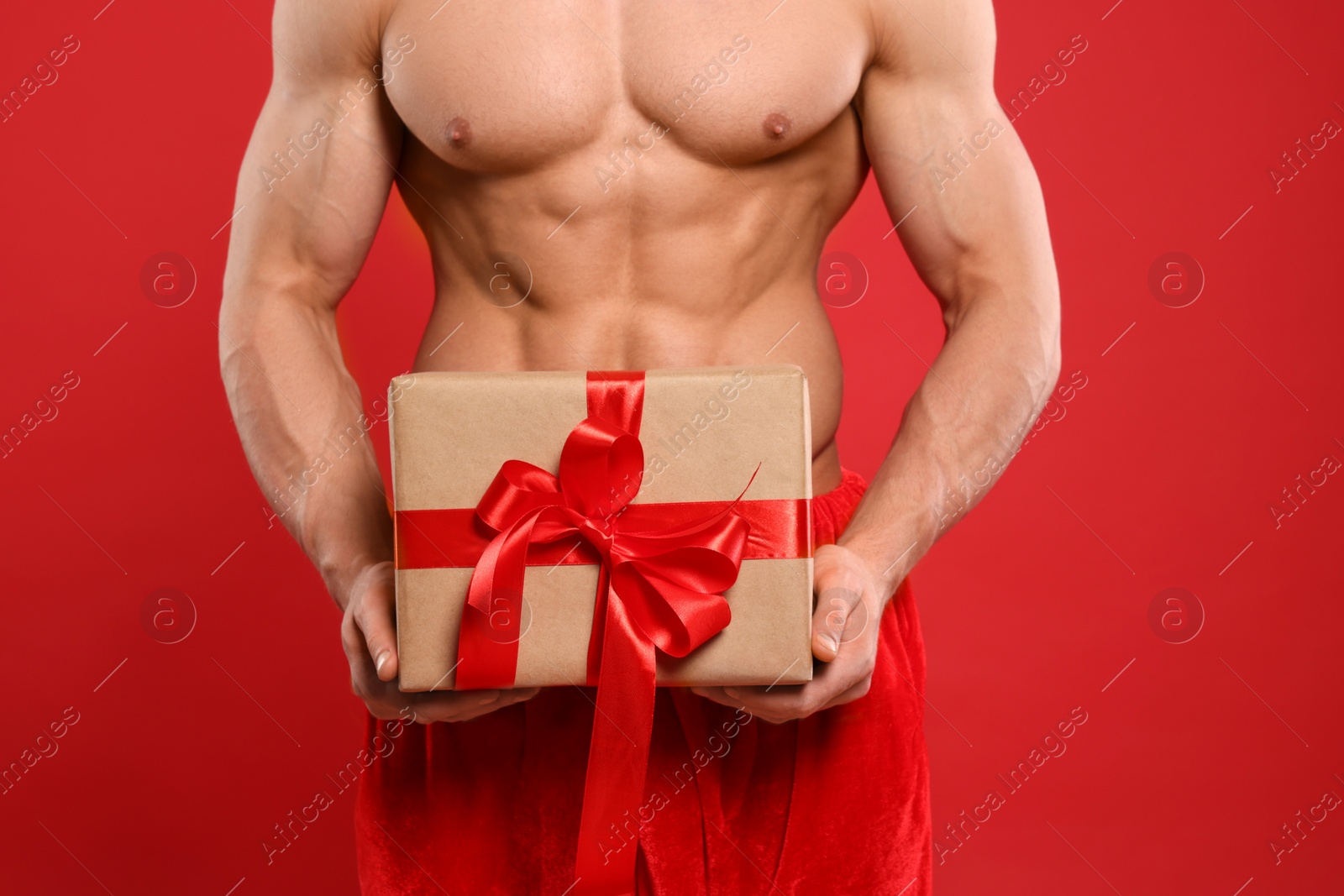 Photo of Young man with muscular body holding Christmas gift box on red background, closeup