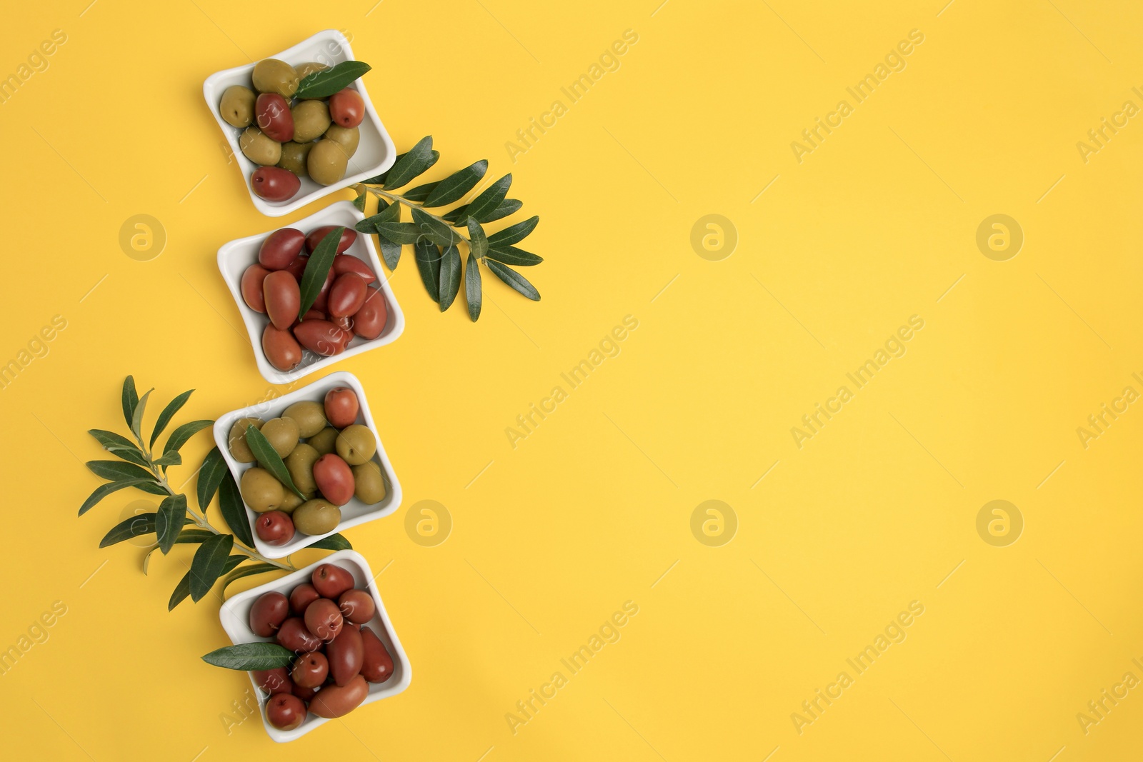 Photo of Different fresh olives and green leaves on yellow background, flat lay. Space for text